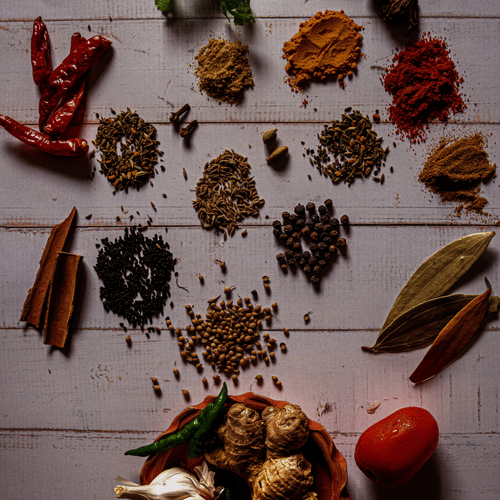 Various spices like tumeric, cinnamon, bay leaves, garlic, and more  laid on a table