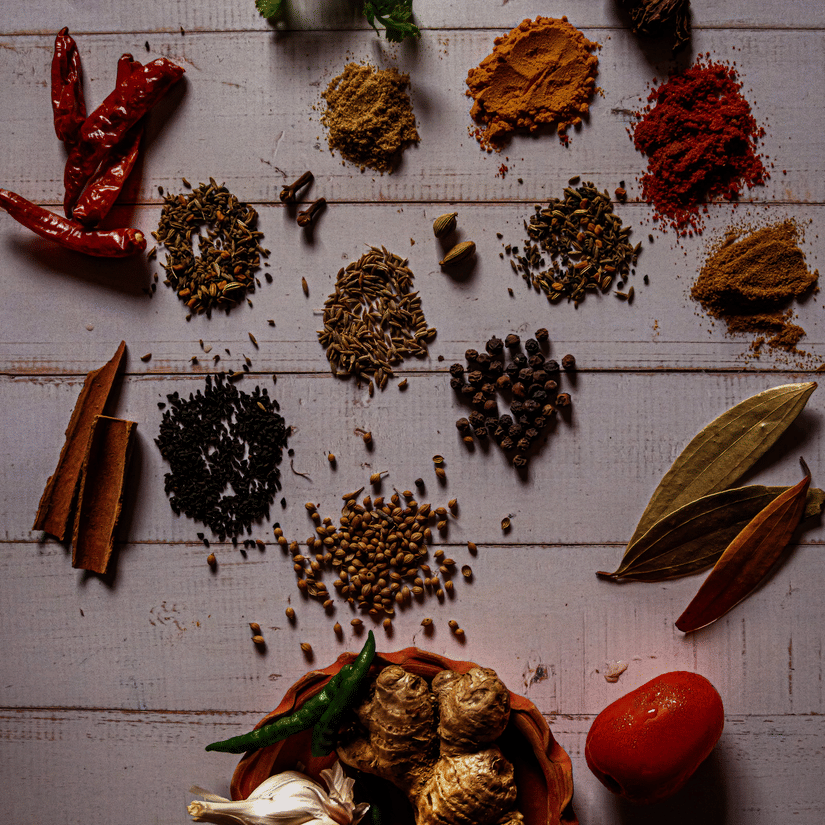 Various spices like tumeric, cinnamon, bay leaves, garlic, and more  laid on a table
