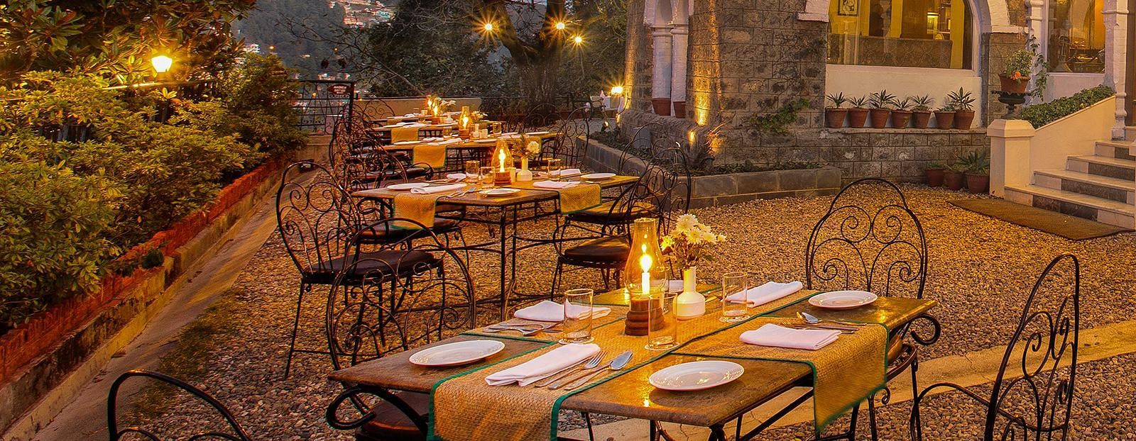 Pairs of tables places with chairs to accommodate up to 4 people on a set, in a outdoor setting in front of a house's entrance.