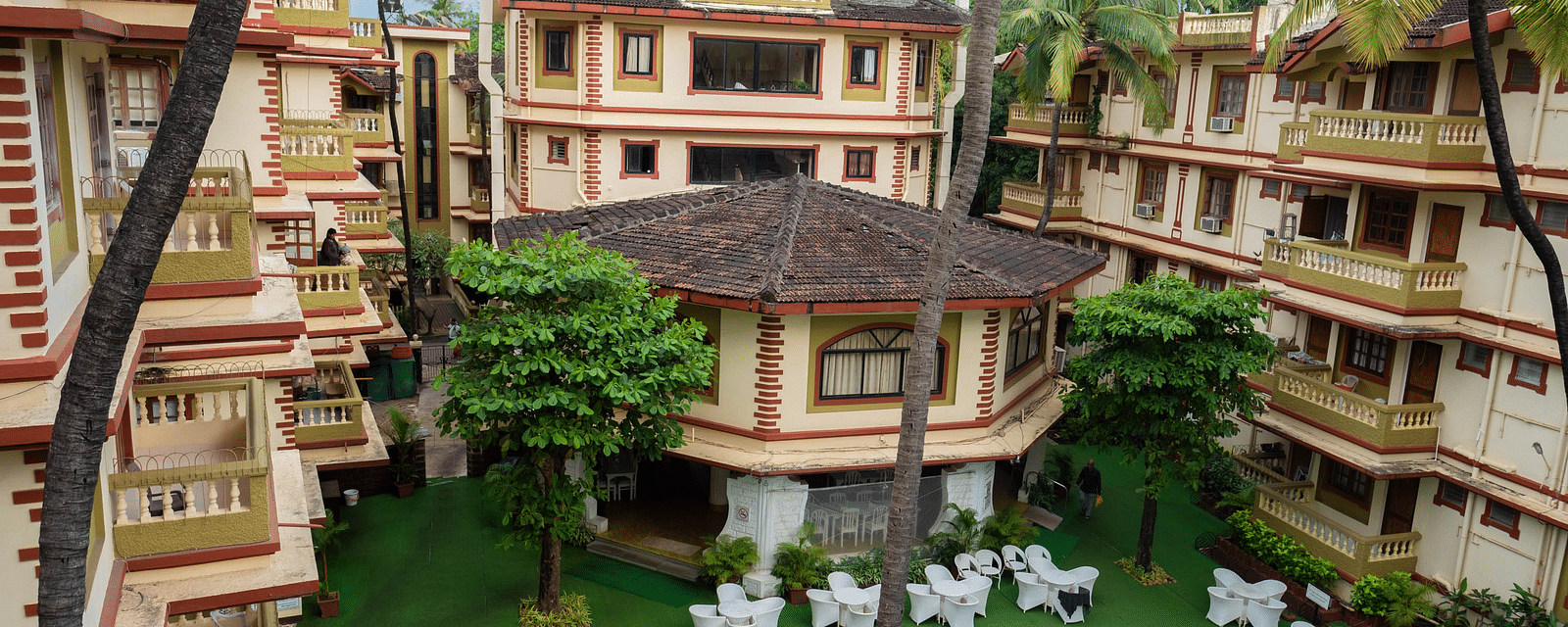 Facade of  Vistar Holidays, Goa with a swimming pool in front and chairs on the side of the pool.