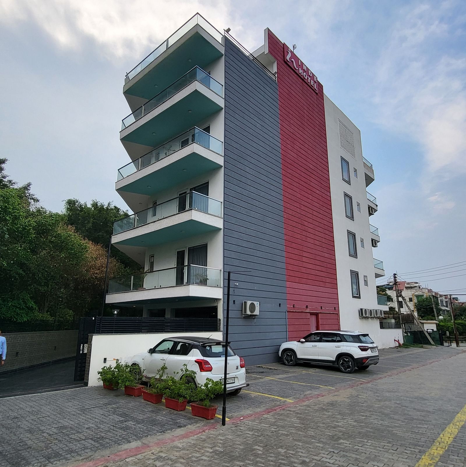 A facade of Inde Hotel Golf Course Extension featuring multiple storeys and balconies on each floor, and cars parked on the lawn