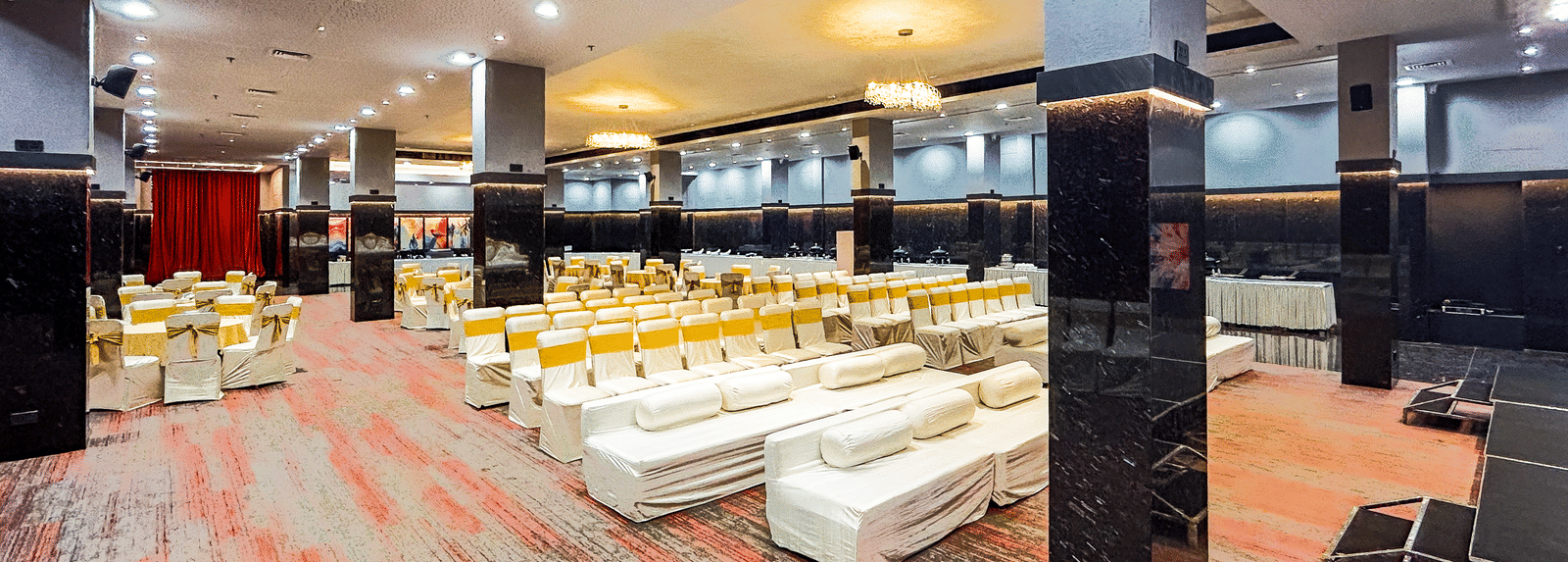 Spacious banquet hall with carpet flooring, sofas, and stage seating at Infiniti Hotel, Indore.
