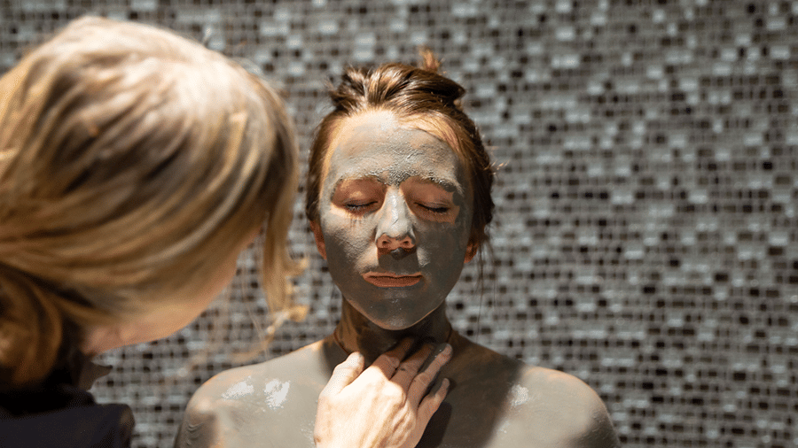 A therapist applying mud to the face and neck of a woman sitting with her eyes closed at YO1 Longevity & Health Resorts, Catskills