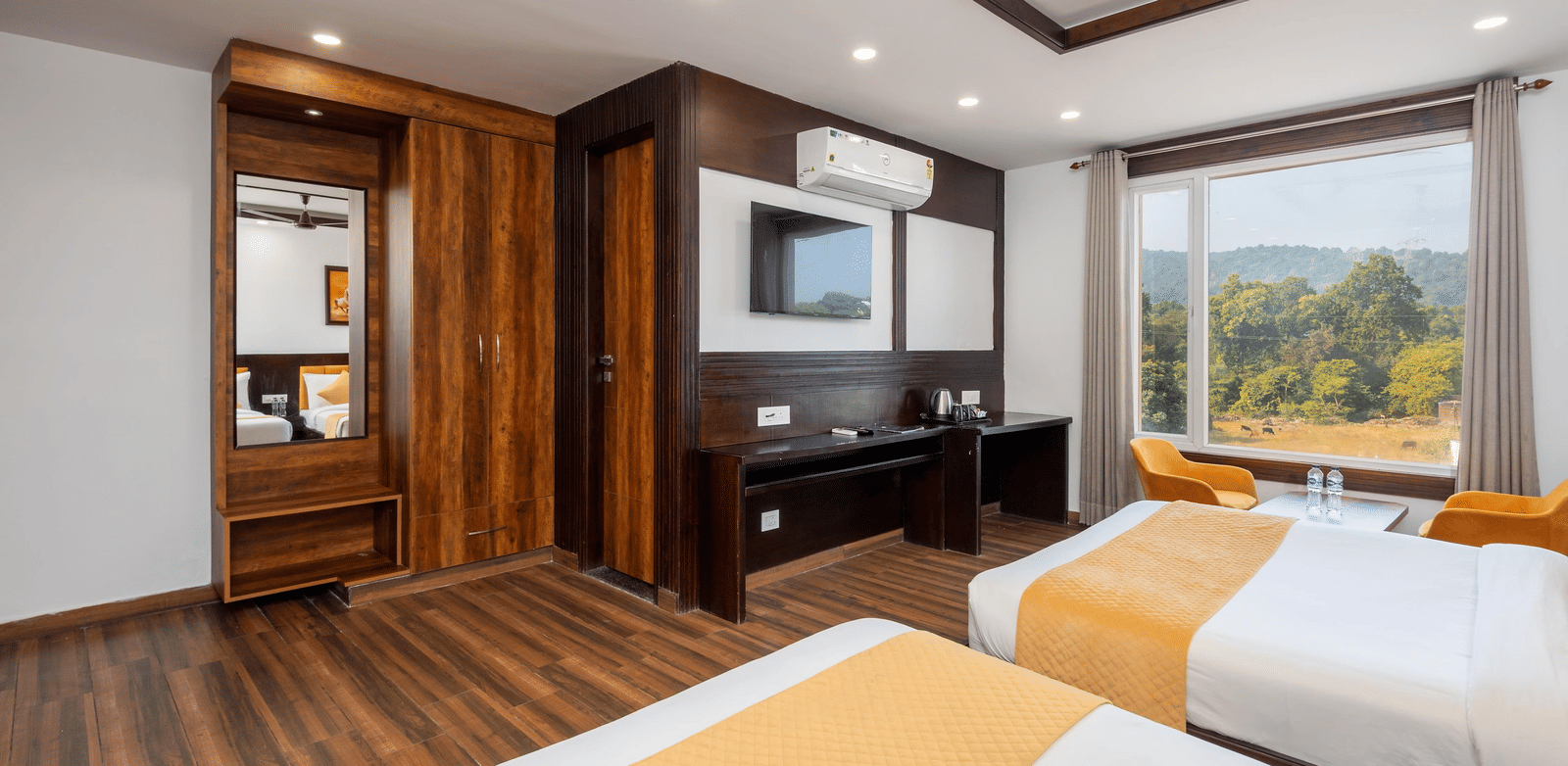 Interior of a room showing beds, a television, wardrobe area, and large window with outside view at Perfectstayz Premium Shanti Heritage, Haridwar.