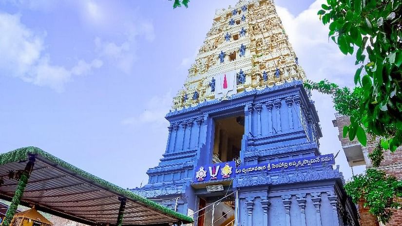 A tall temple tower with intricate architecture, viewed from below with lush green trees surrounding it
