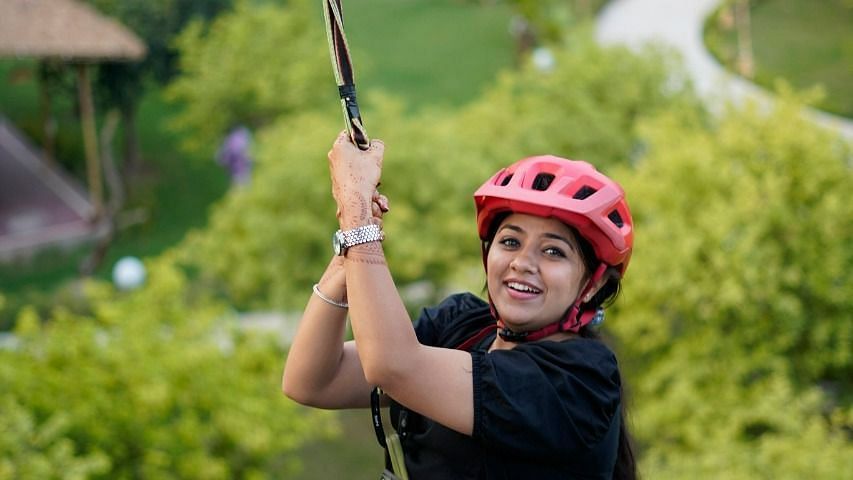 Woman on a zipline ride at inflated trampoline surrounded by trees at Themis Mudhouse - A Nature's Retreat Resort & Wellness