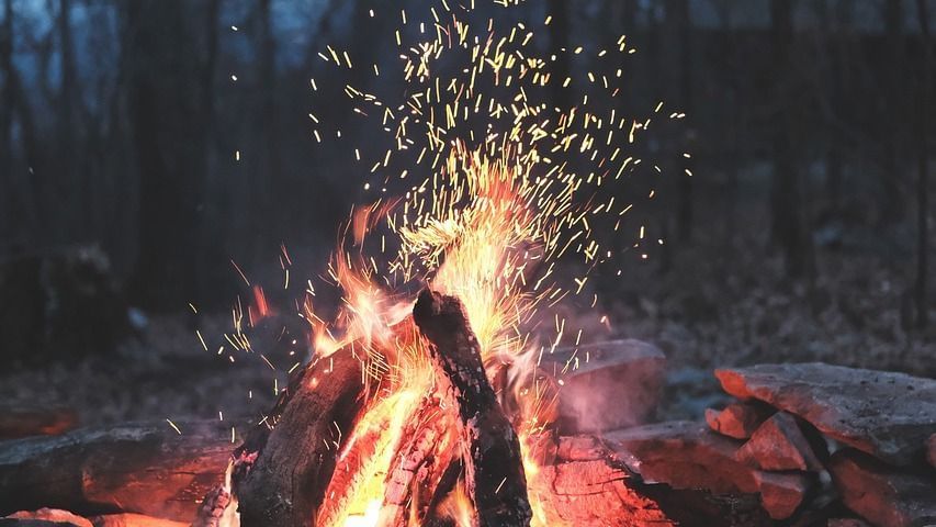 a bonfire surrounded with rocks with a misty forest in the background