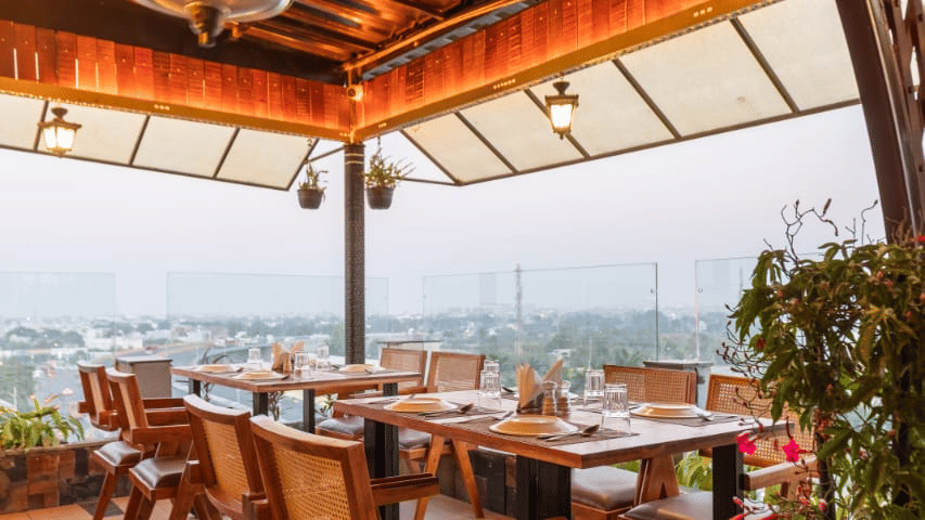 The Hills View restaurant at The Papaya Tree Hotels offering an open terrace dining area with wooden tables and scenic outdoor views, perfect for enjoying meals in a relaxed natural setting.