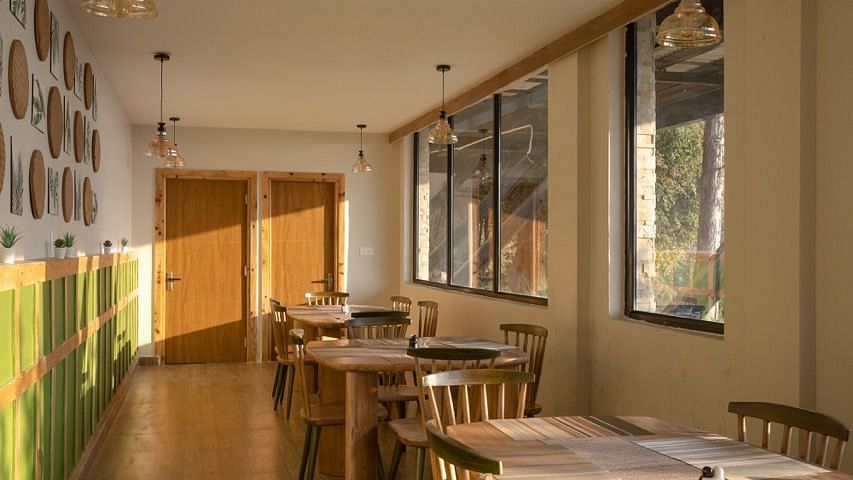 An image of a dining area with several chairs and table placed at one side with widows| Avalon Cottages, Kanatal