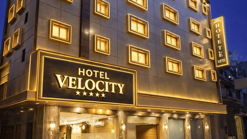 Exterior night view of Hotel Velocity building with warm illuminated windows and signage.