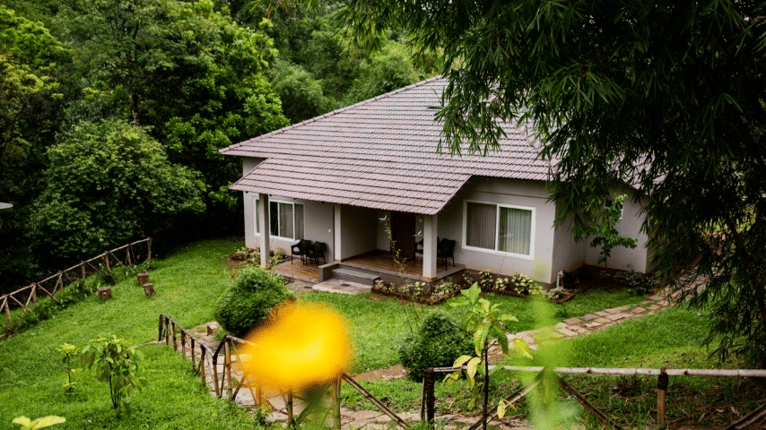 A cottage surrounded by lush greenery, with yellow flowers blooming.- Abad Brookside Lakkidi, Wayanad