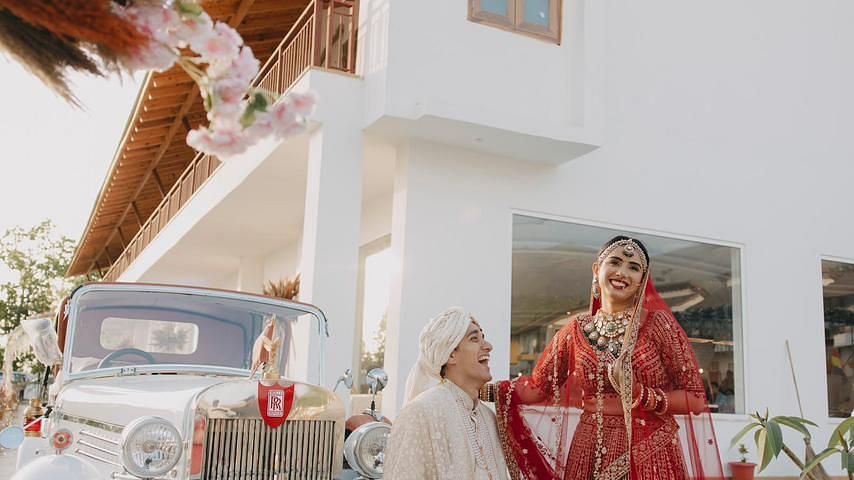 A bride and groom posing for a photo in front of a vintage car.