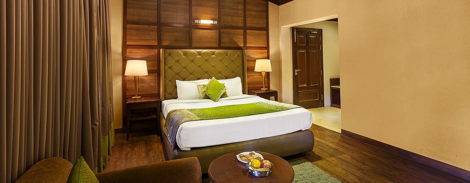 a bedroom with a large bed and side lamps, a table and a sofa - The Earl's Court, Nainital