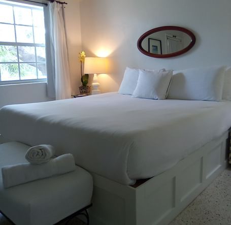 Bed at Casa Morada with white linens, towels on a bench at the foot, and a window with curtains in the background.