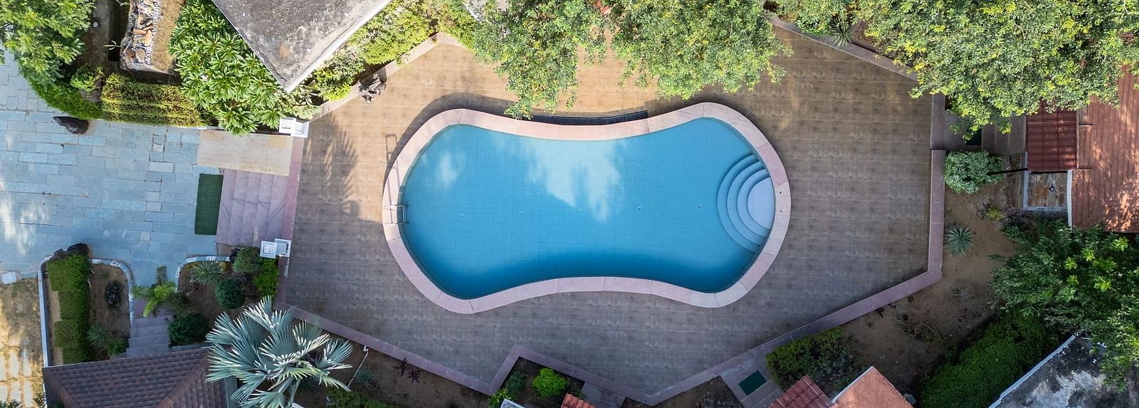 Aerial view of a swimming pool at Valley by Grassfield, nestled among lush trees and surrounded by accommodations.