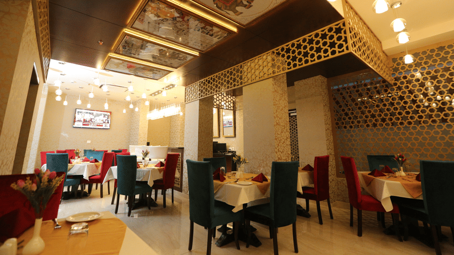 A dining area at Comfort Inn Sapphire by Eastlynn Collections, Jaipur with multiple tables, chairs, ceiling design, and wall patterns.