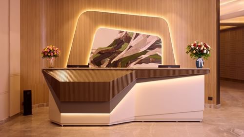 A modern reception desk with a lit backdrop at Riviera Sarovar Portico, Pathankot.