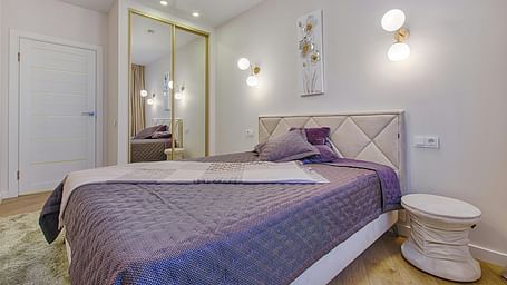 Stylish hotel room showcasing a bed with plush pillows, mirrored closet doors, wall lighting, and minimalist decor.