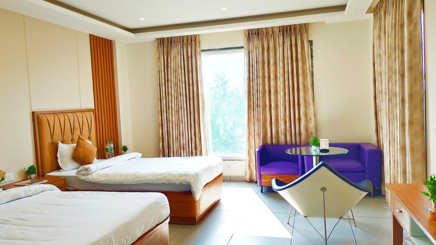 Executive Room at The Prince ZENQ Xpress Resortt Rohtak with two twin beds featuring wooden bases, a bright window with light brown curtains, a purple sofa, and a white chair.