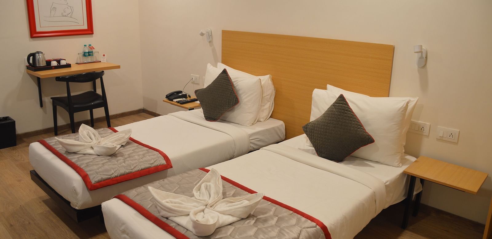 A bedroom featuring two single beds and a small work desk and chair in the corner - Lords Eco Inn Belagavi