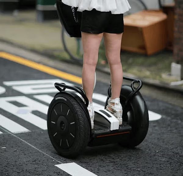 A woman riding a Segway on an empty road captured from behind as she moves forward.