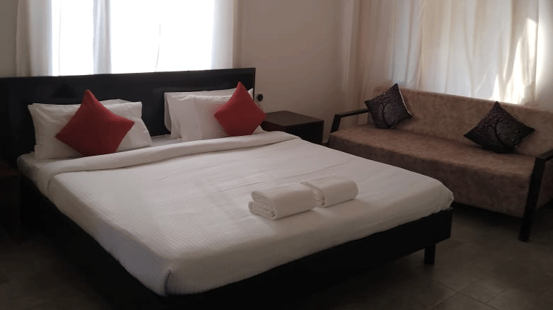 Guest room featuring a king size bed with red cushions, a sofa seating area and curtained windows.