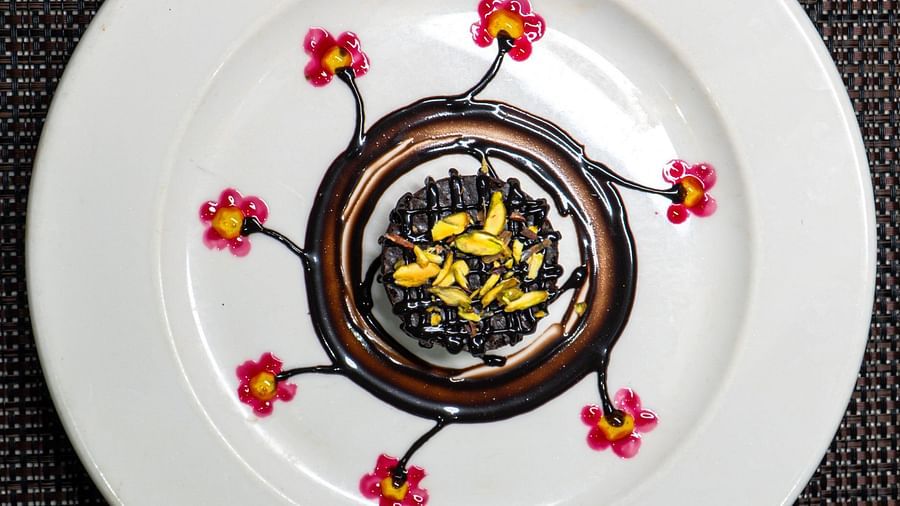 A plate with a circular dark dessert decorated with light elements.