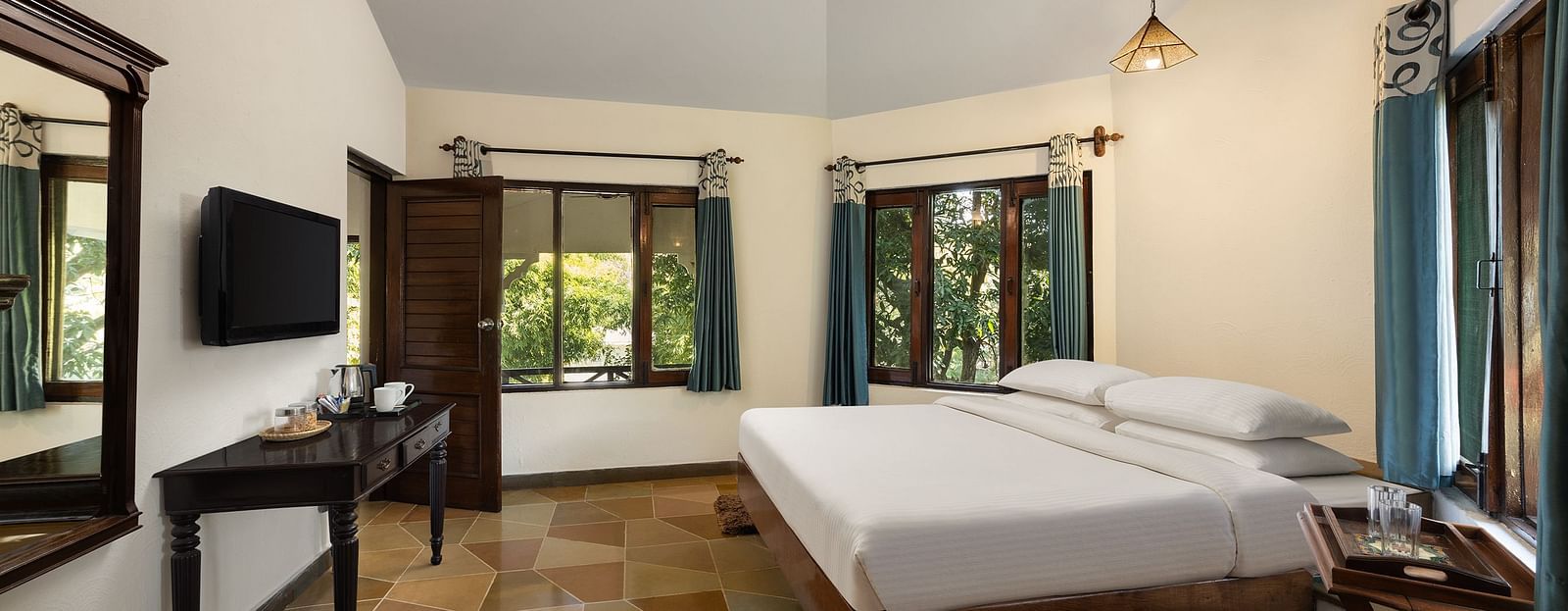 An image of a bedroom with double size bed, bedside table on either side, photos hanged on the wall and four windows from which natural lights are coming in - The Riverview Retreat,  Corbett