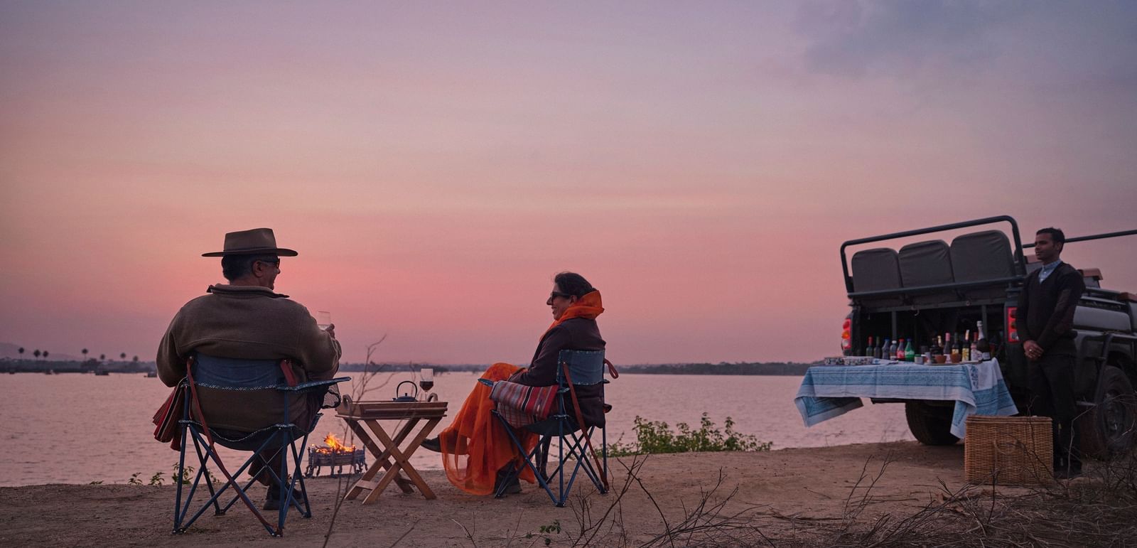 couple soaking in the pink hues of the sunset with a picturesque lake in front of them at dev shree , deogarh