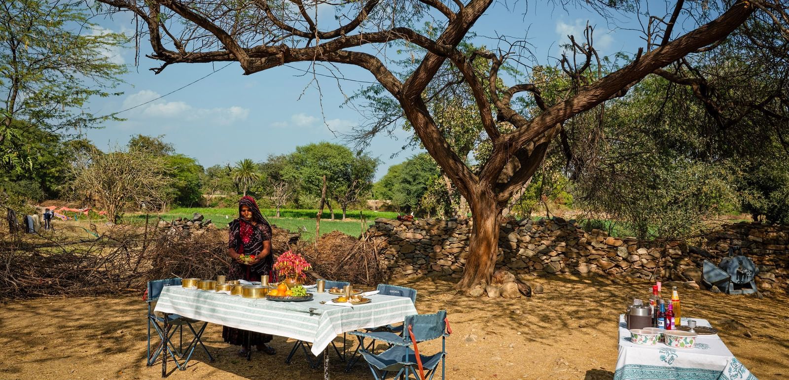 image of a woman dressed in traditional outfit serving various rajasthani delicacies on the table at dev shree, deogarh