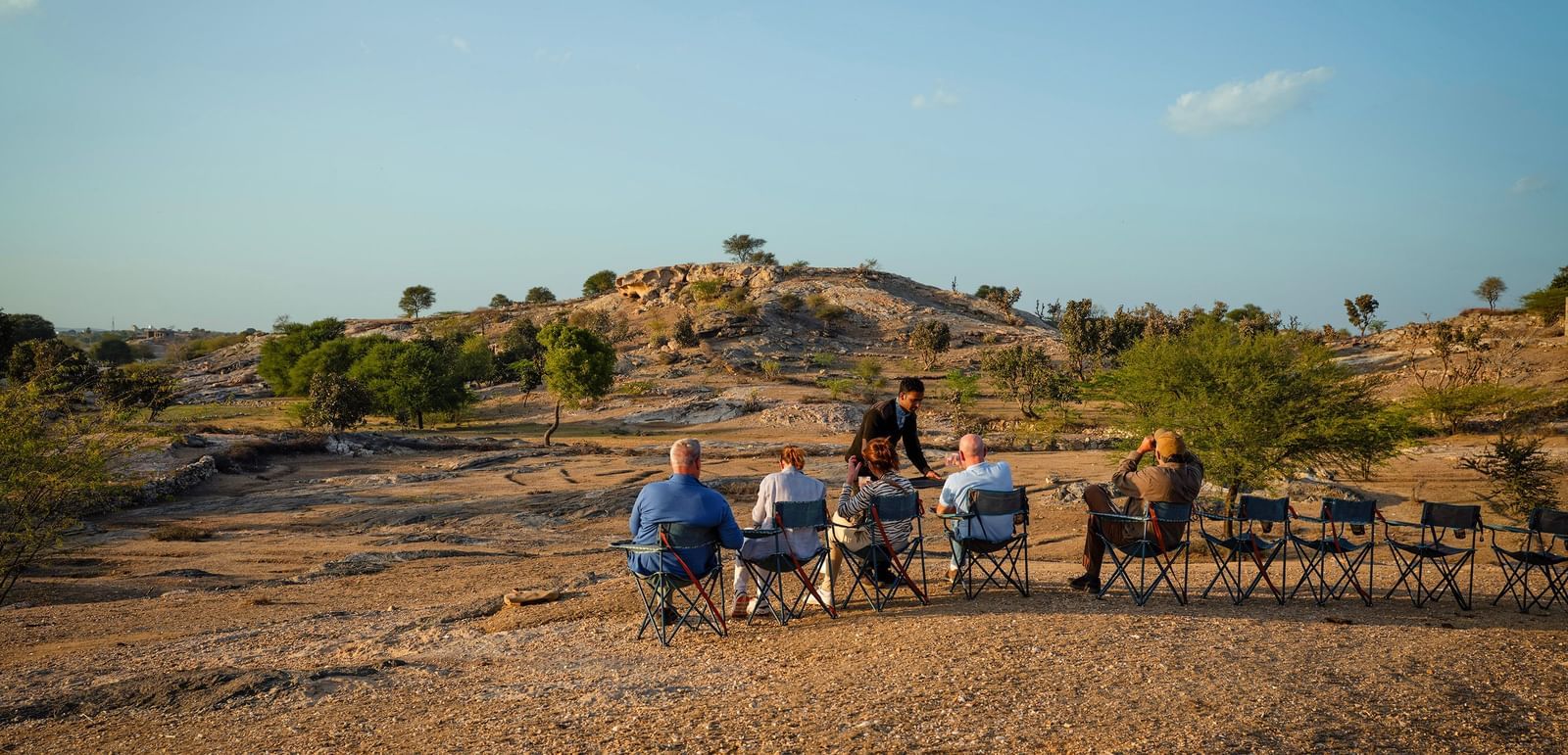 image of a few people sitting on chairs lined up in a rocky desert like area with very less green cover