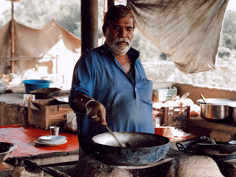 Cook preparing food over a traditional stove at a rustic roadside dhaba.