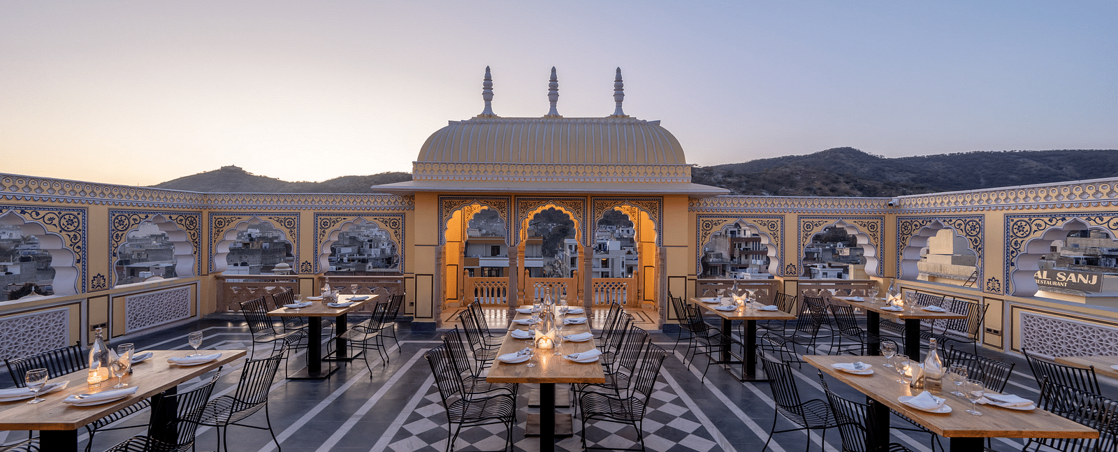 a roof top dining setup with beautiful views of the surrounding mountains and the early sunset - Brij Castle, Jaipur