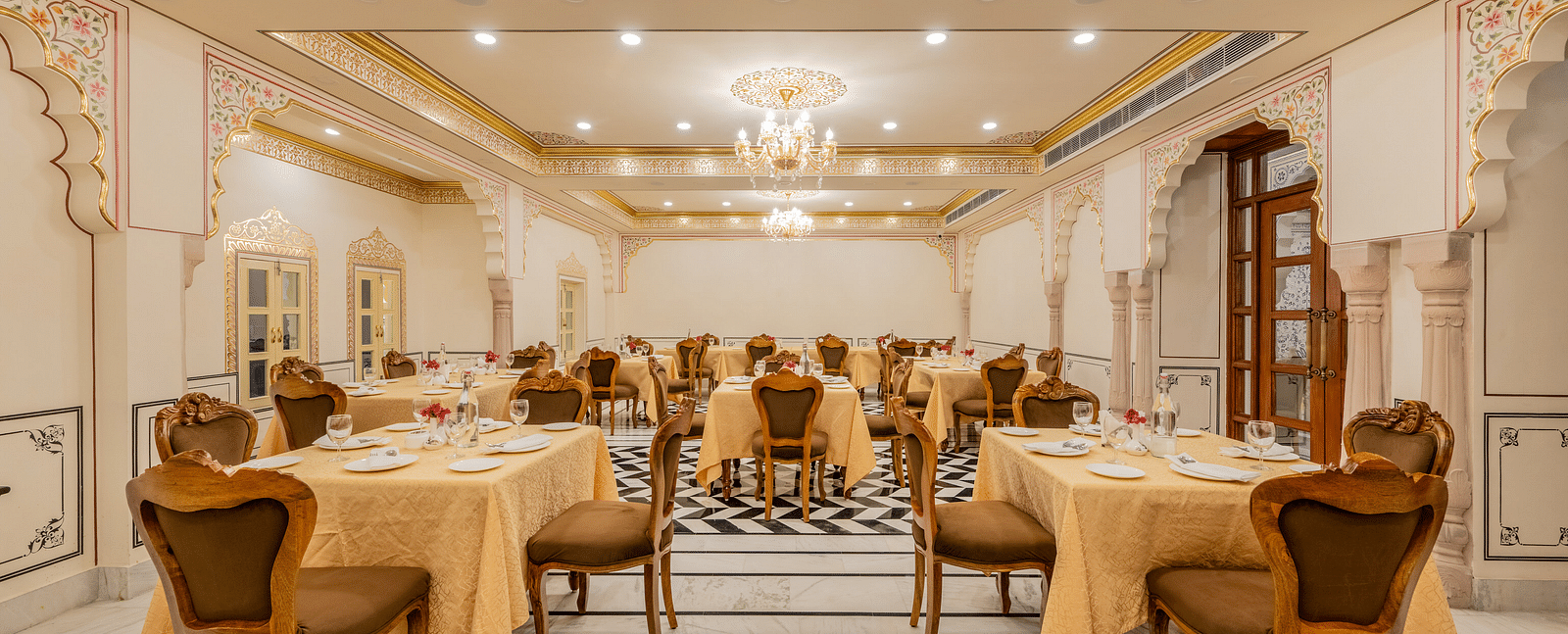 a well arrnaged dining setup in our indoor restaurant with black and white tiles and elegant furnishings - Brij Castle, Jaipur