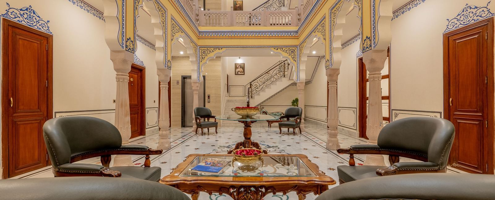an expansive brightly lit lobby area with a common seating area with four leather chairs surrounding a square table top - Brij Castle, Jaipur
