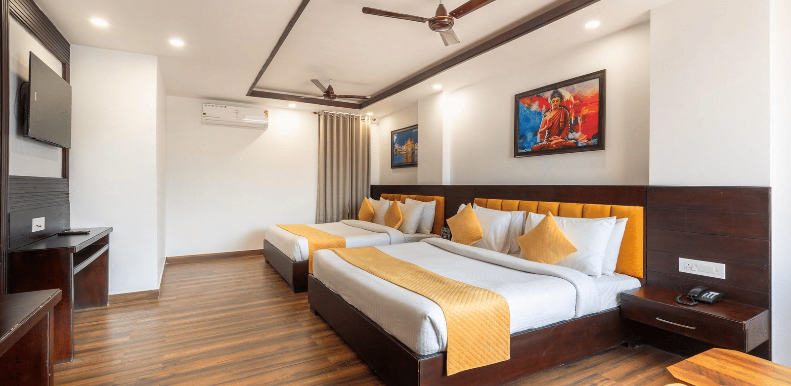 2 large beds, a television, ceiling fan, and 2 artworks in a hotel room at Perfectstayz Premium Shanti Heritage, Haridwar.