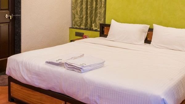 A close up shot of  wooden bed frame, white linens, a lime green accent wall, and an air conditioning unit.