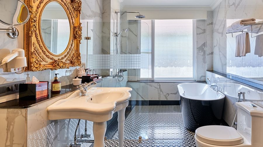 Luxurious bathroom of Imperial Villa with a porcelain sink, gold framed mirror, standalone bathtub, glass door shower, patterned flooring  and a commode