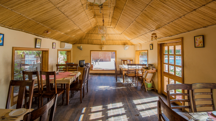 An indoor dining space featuring multiple wooden tables and chairs under a sloped bamboo-textured ceiling at Garh Govind.