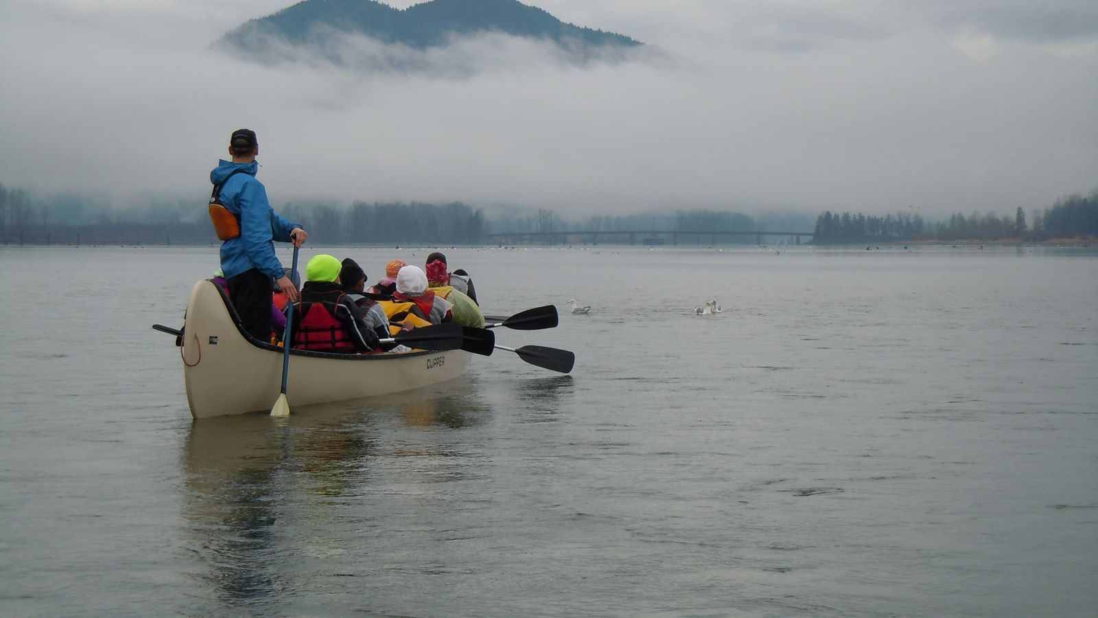 A paddle boat on a large water body with the mountains in a distance with mist hung low over it.