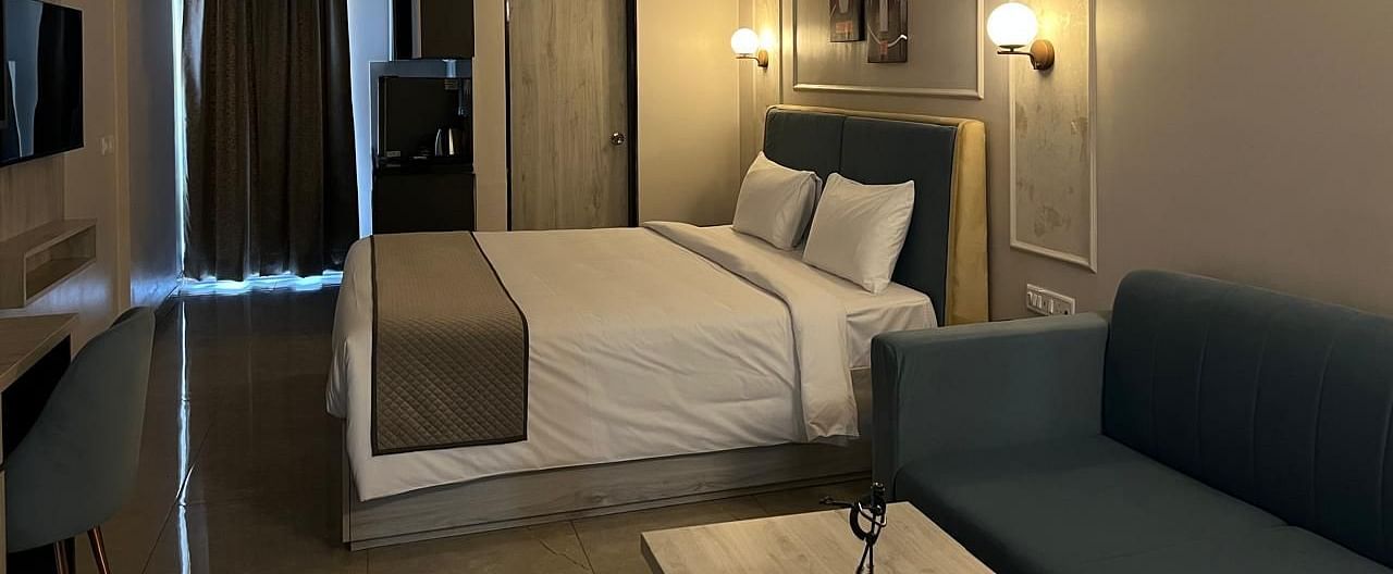 A side view of the room featuring a large bed, warm lighting, and a pathway with sheer curtains at Urban Suites by BluSalzz, Jaipur.
