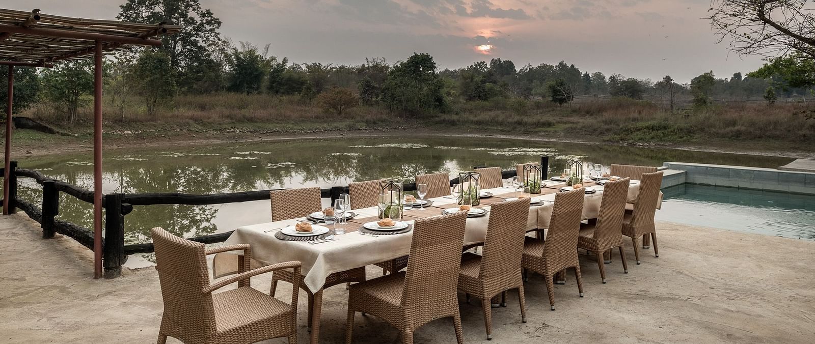 A dining table and multiple chairs arranged neatly near pool at Saccharum Safari Lodge, Balaghat