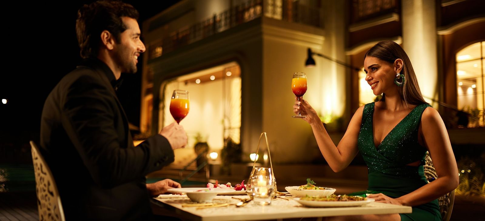 A couple having a candle-lit dinner as they are about to clink their wine glasses at the Imperial Goa.