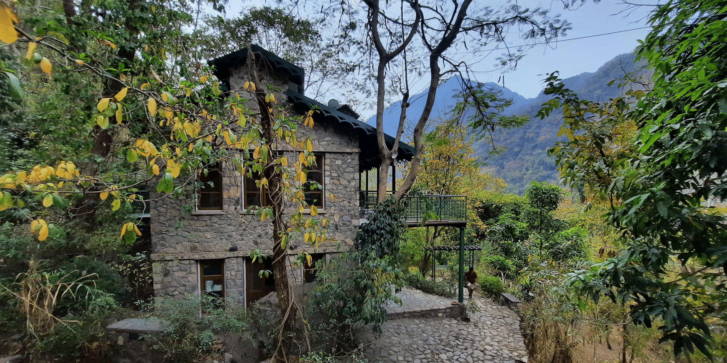 Facade view of Neemrana's Glasshouse on the Ganges amidst the nature with mountains and clear blue sky in the background.