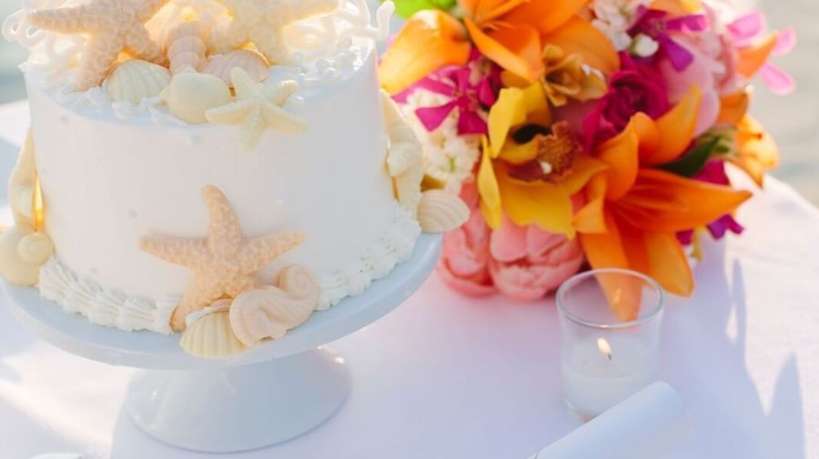 A wedding cake decorated with starfish sits next to a vibrant orange and pink bouquet on a white table at Casa Morada.