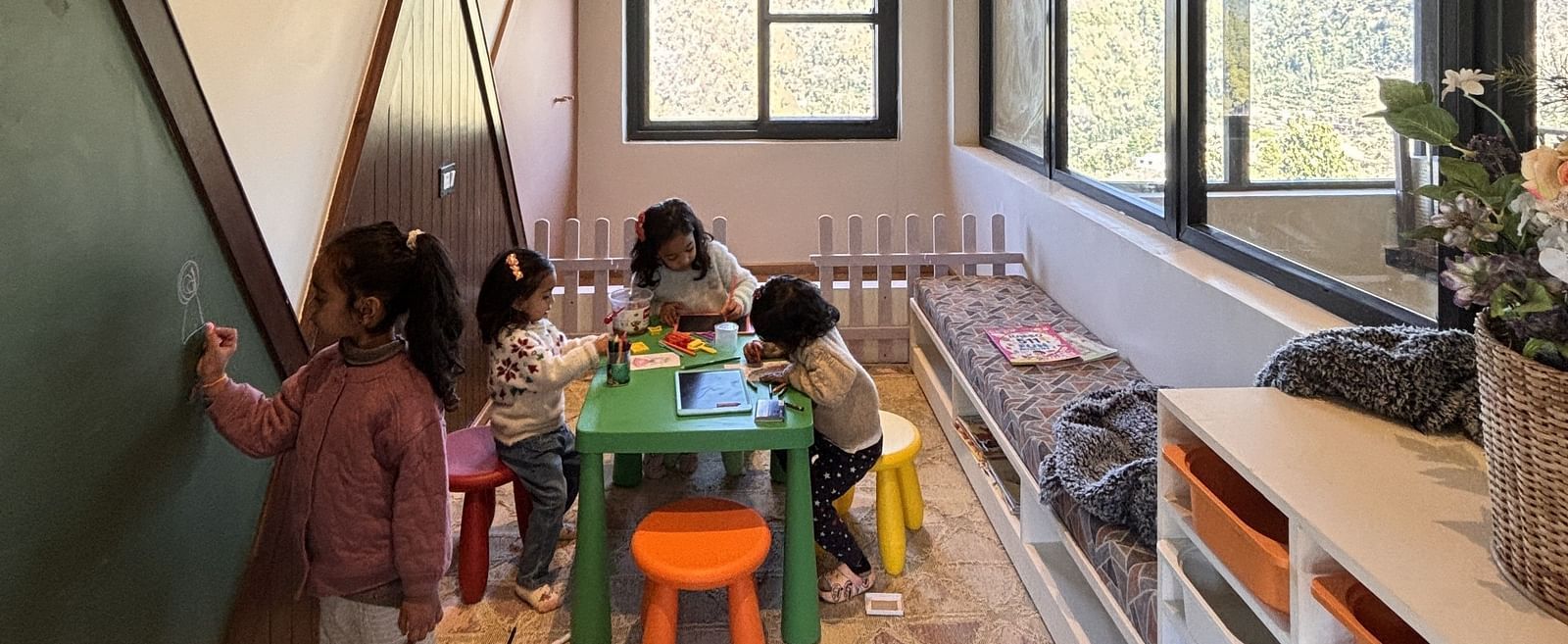 A spacious room at The Chamomile Estate, with three children gathered around a small table playing, while another child writes on the wall-mounted board.