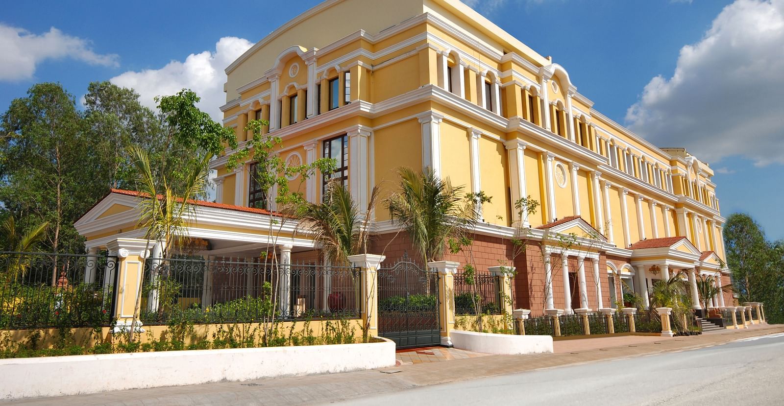 An image of a hotel with an elegant entrance gate, small shrubs lining the pathway, and a lush garden in the foreground