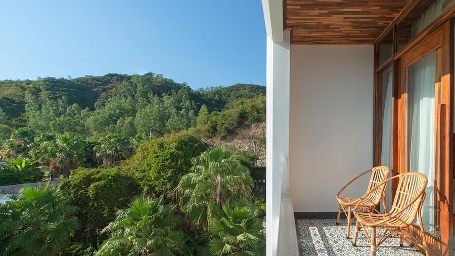 A balcony in one of the rooms at our hotel with a view of lush greenery surrounding it and comfortable chairs to rest upon - Alibu Resort Nha Trang