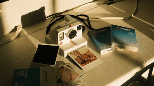 A flatlay image of polaroid camera with a snapshot coming out of it next to which the polaroid papers are placed in a couple of packets
