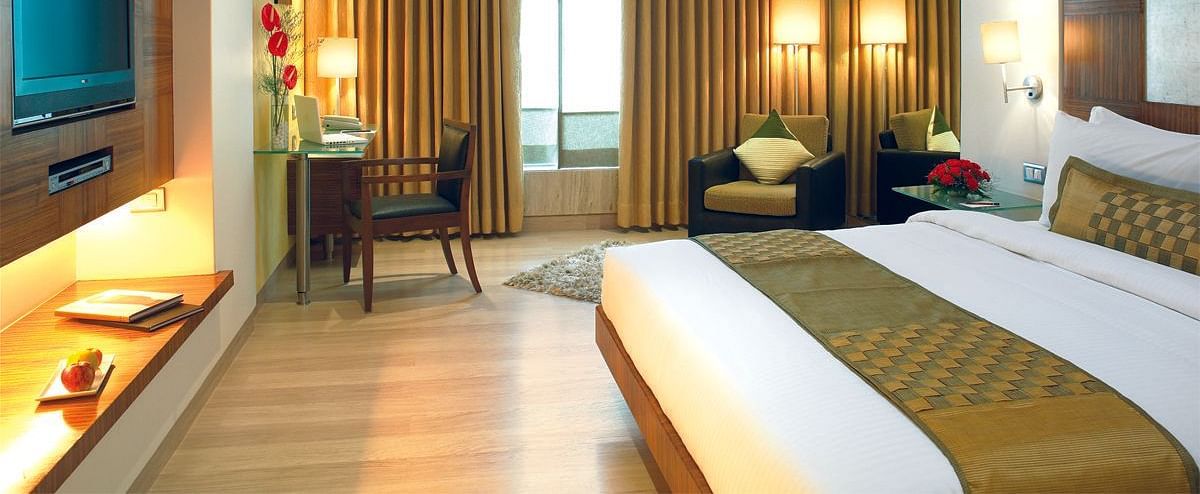 Image of a the executive room featuring a king size bed, a study table and chair, flat screen television, and an expansive window with golden curtains. | Mirage Hotel